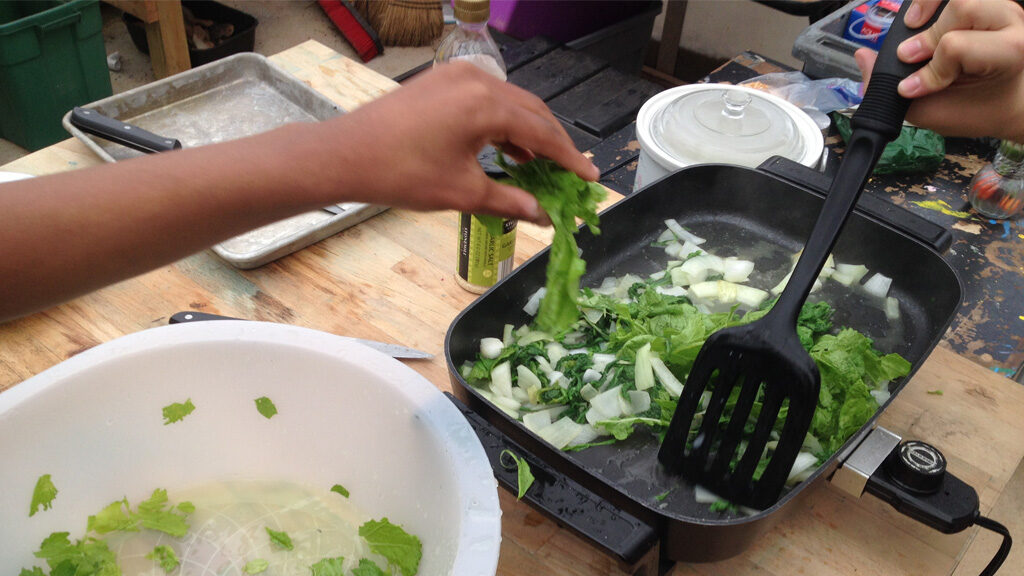 People cook onions and greens in an electric griddle.