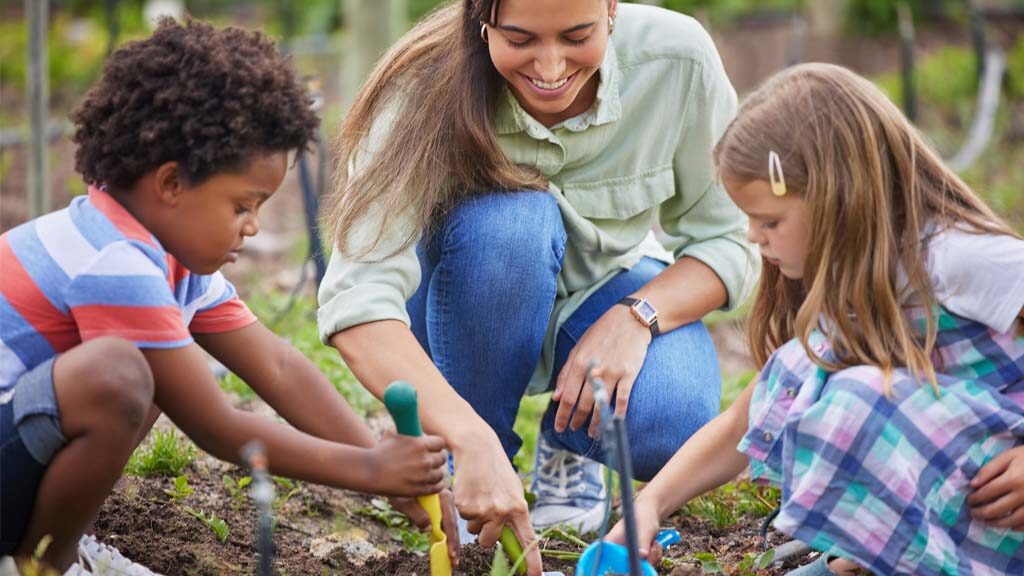 Children dig in the garden with an adult.